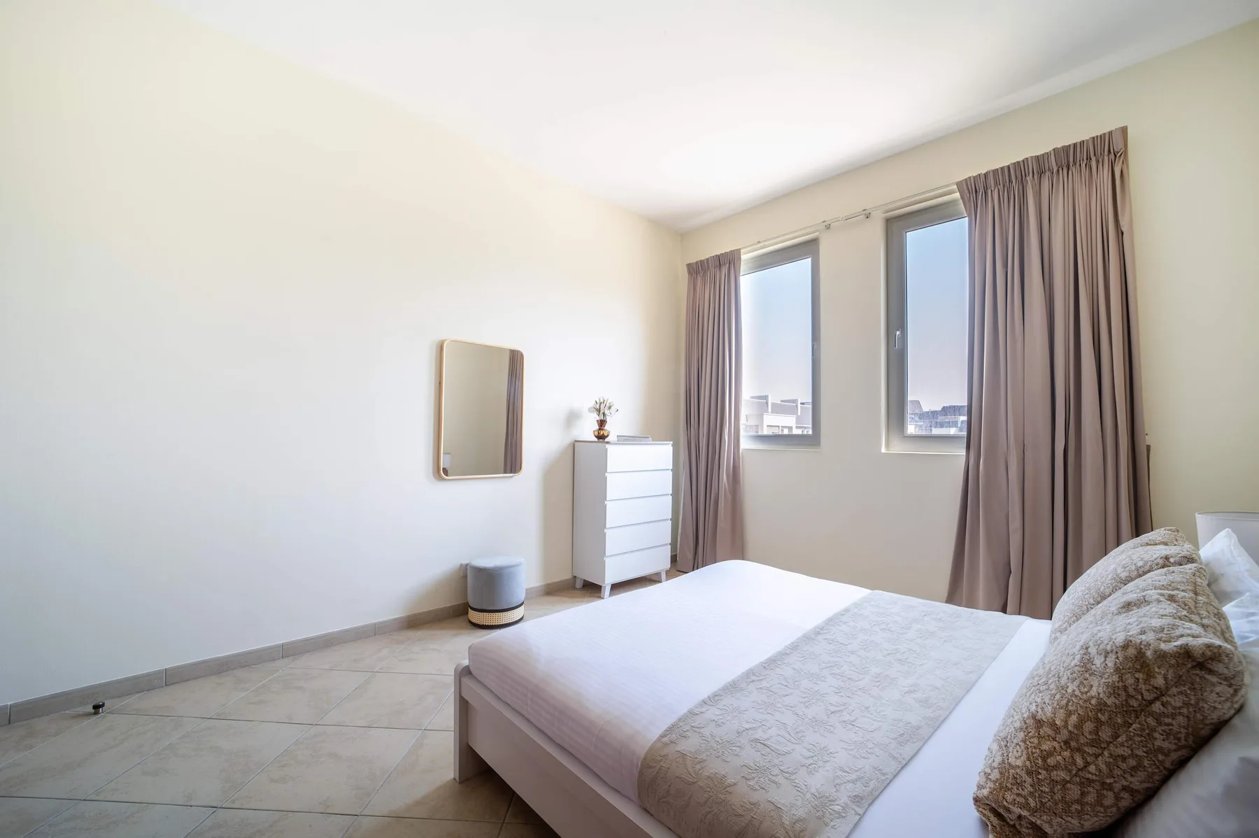 A bright bedroom with a bed, dresser, and tall curtained windows.