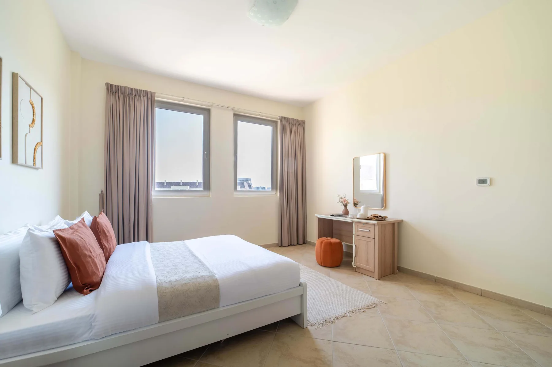 A bright bedroom with a bed, curtained windows, and a small desk.