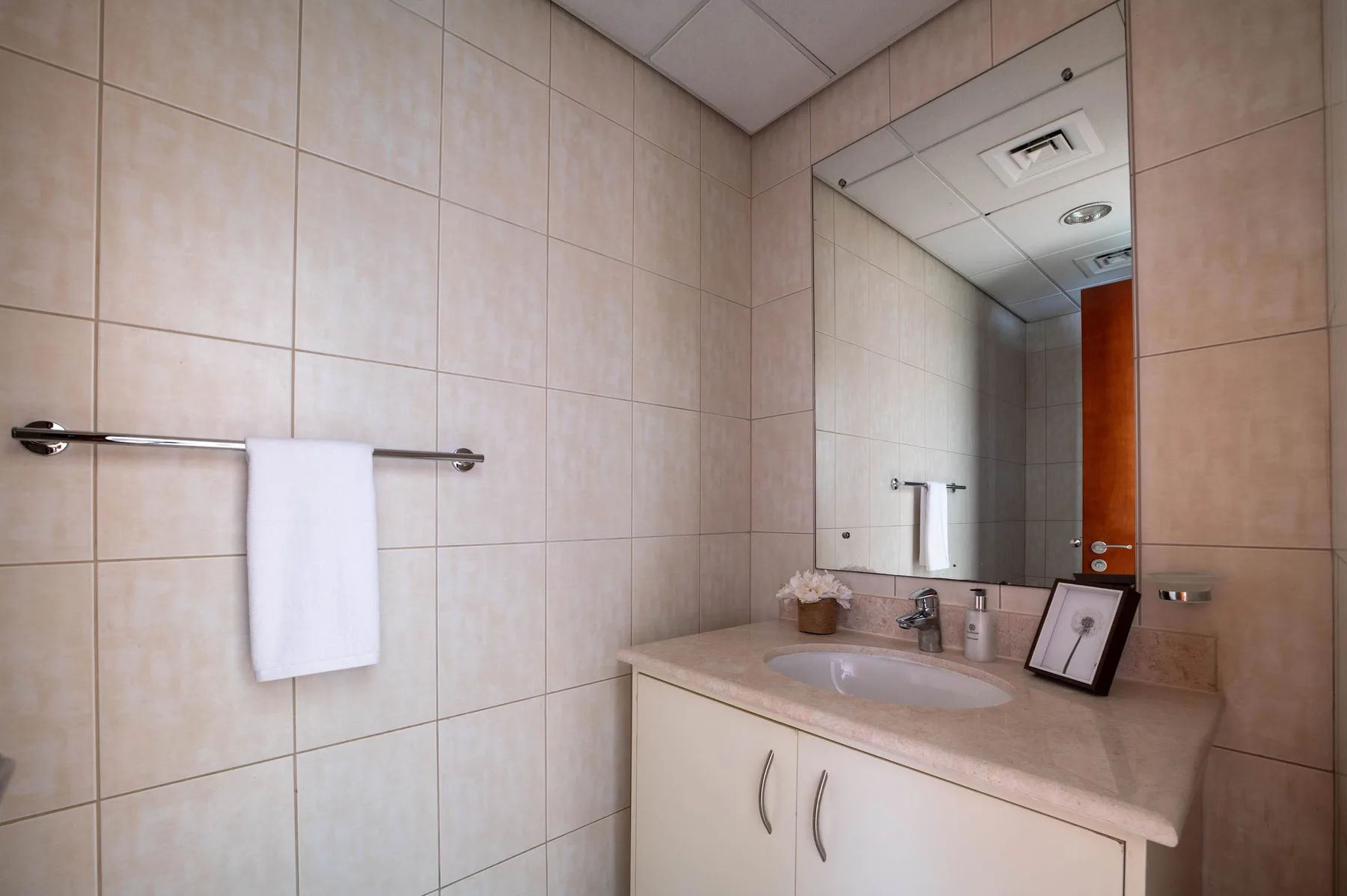 A tiled bathroom vanity with a sink, mirror, and towel rail.
