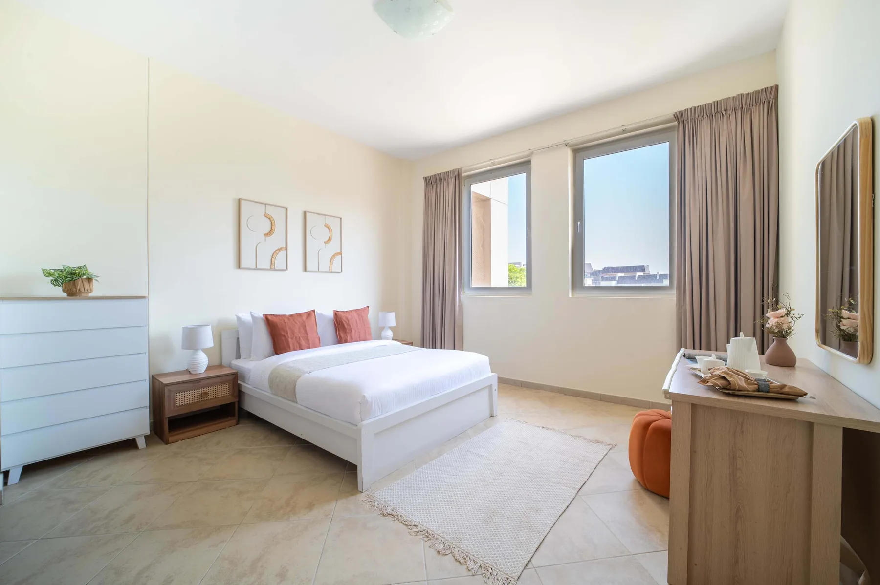 A bright bedroom with a white bed, framed art, and large windows.