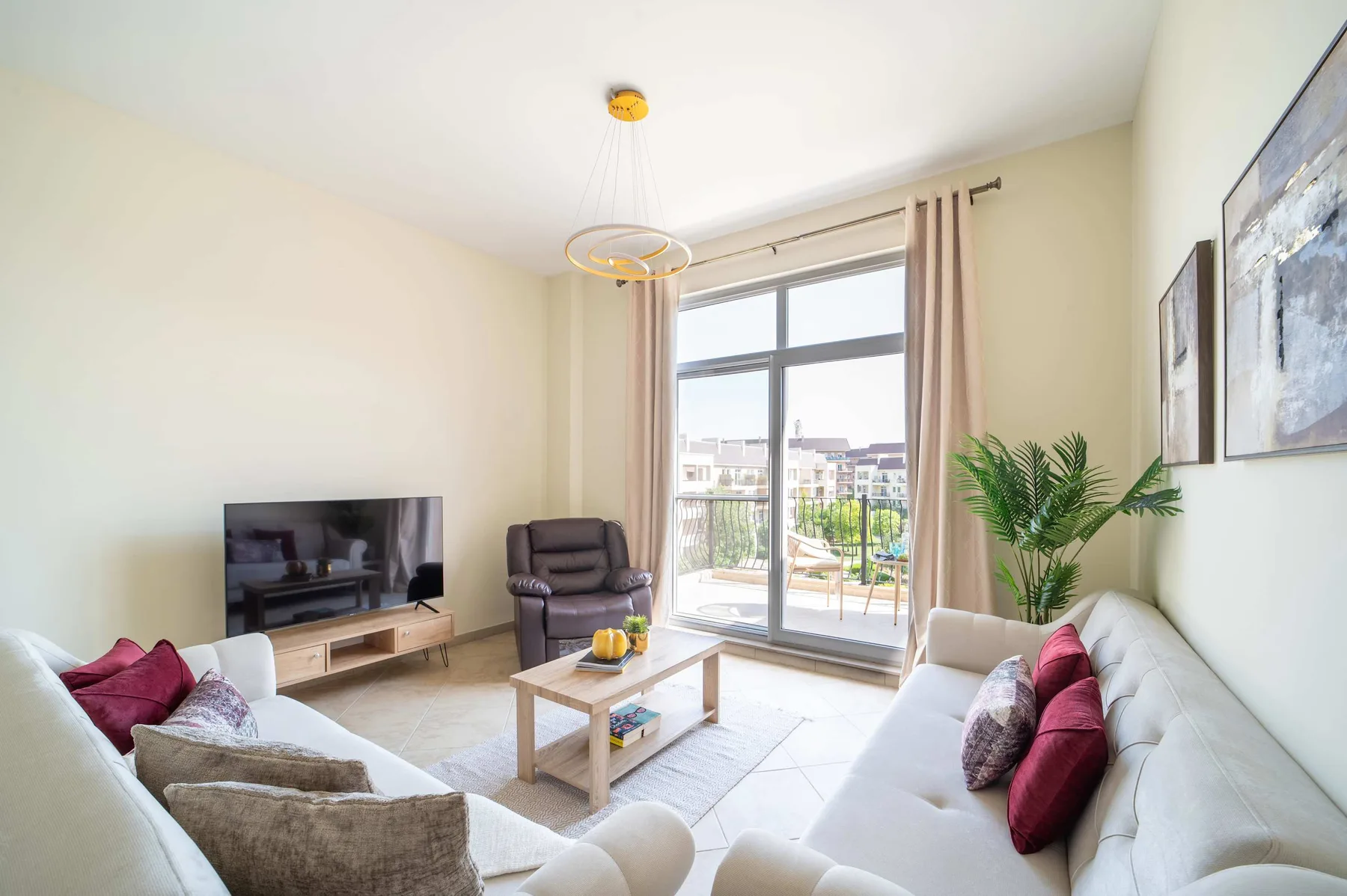 A bright living room with seating, a television, and a large window opening onto a balcony.