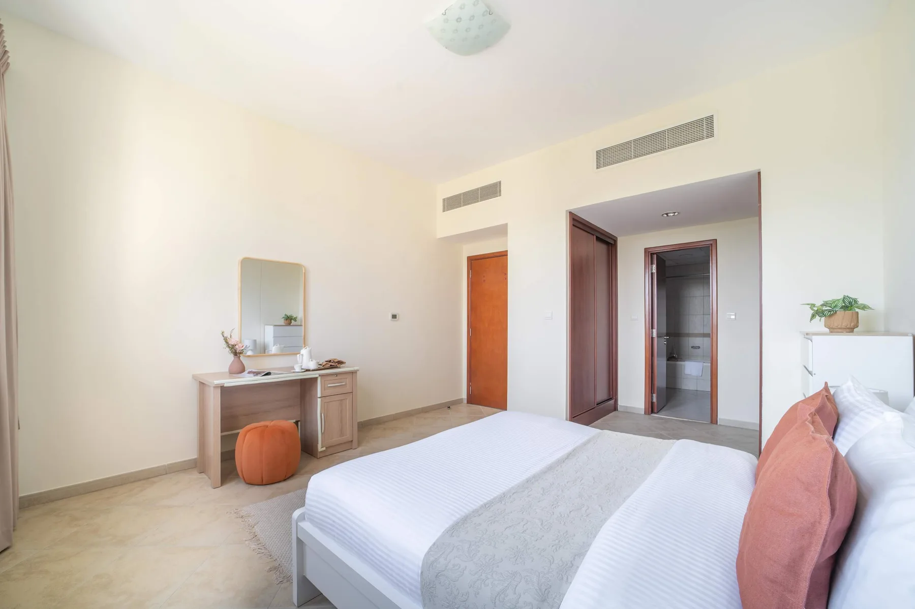 A bright bedroom with a bed, vanity, and open doorway.