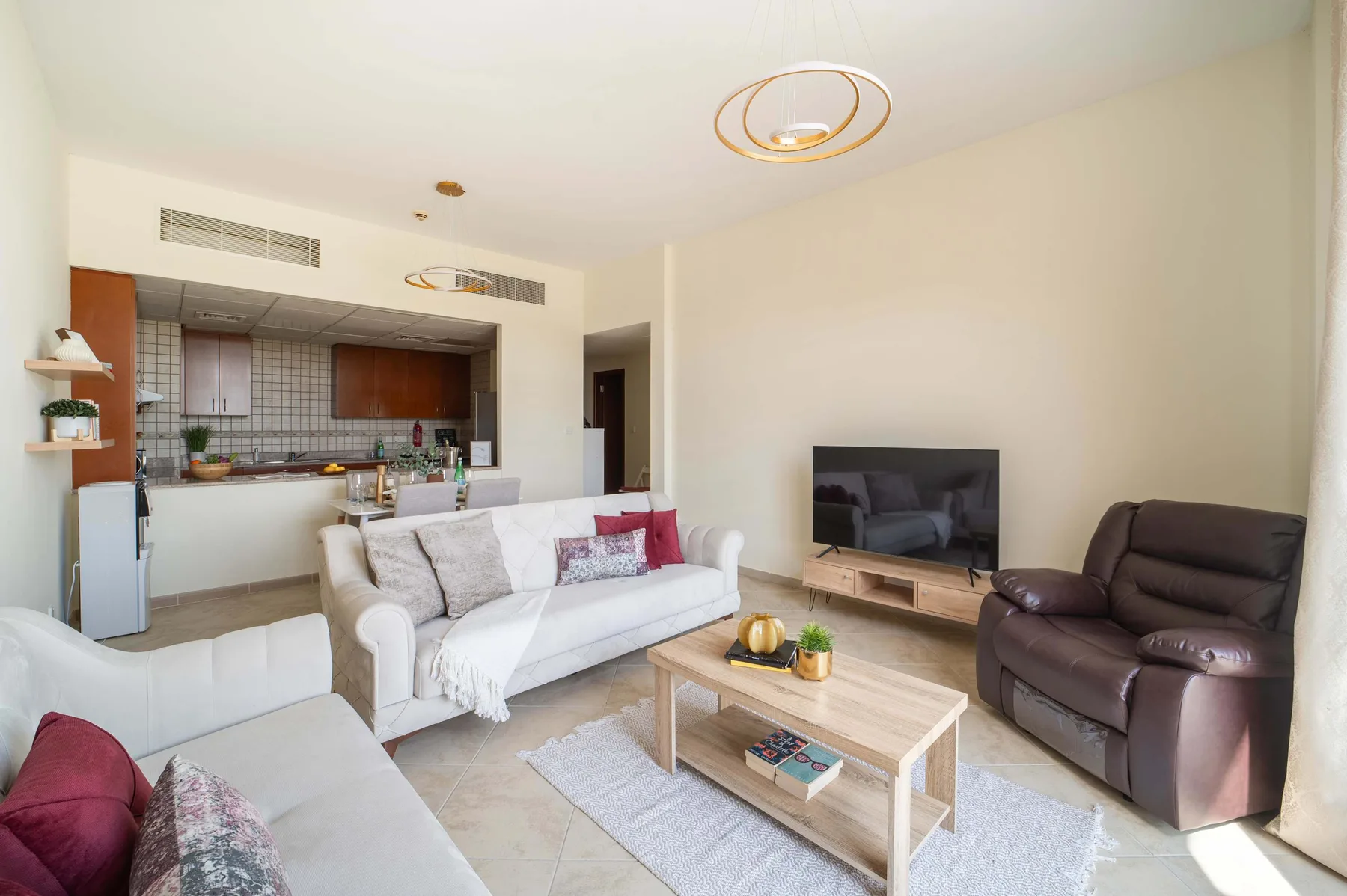 A bright living room opens onto a kitchen, with sofas and a television.
