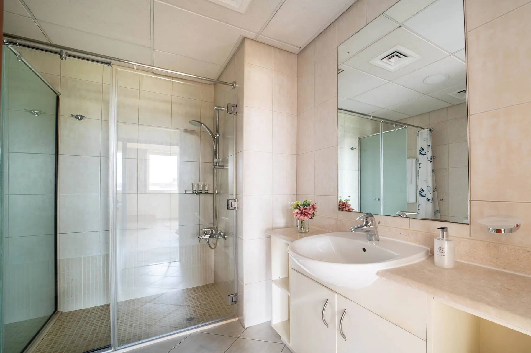 A tiled bathroom with a glass shower and a sink beneath a large mirror.