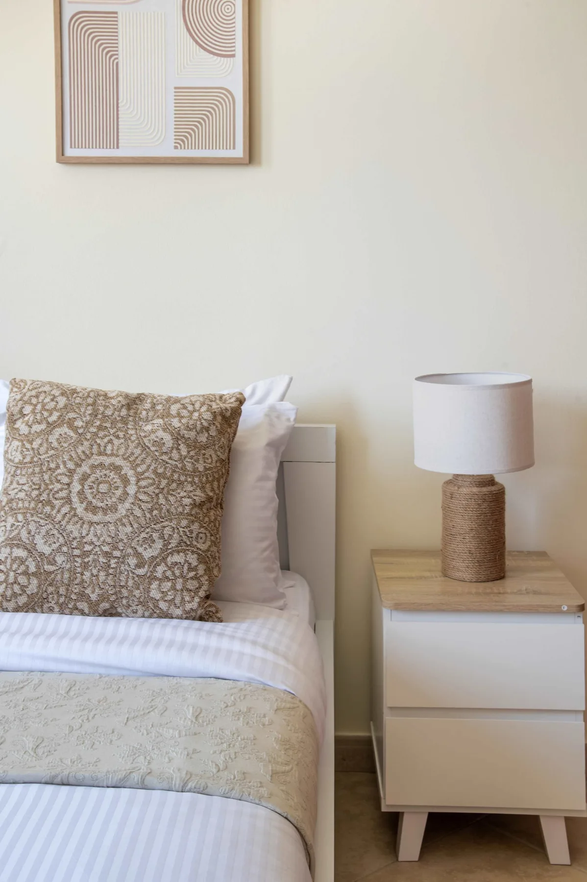 A bedroom with a neatly made bed and a bedside table topped by a lamp.