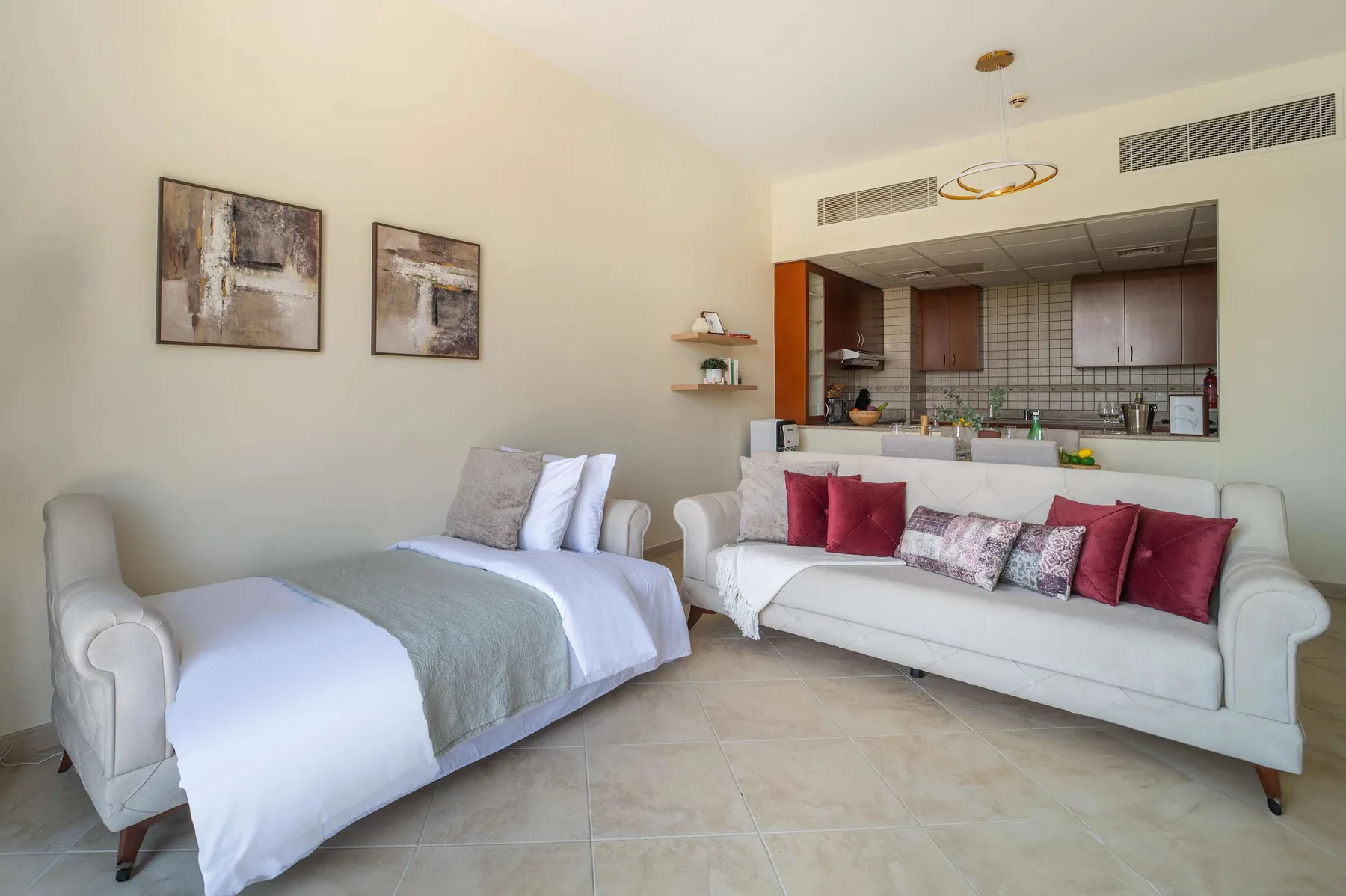 A living room with white seating, decorative pillows, and an open kitchen behind it.