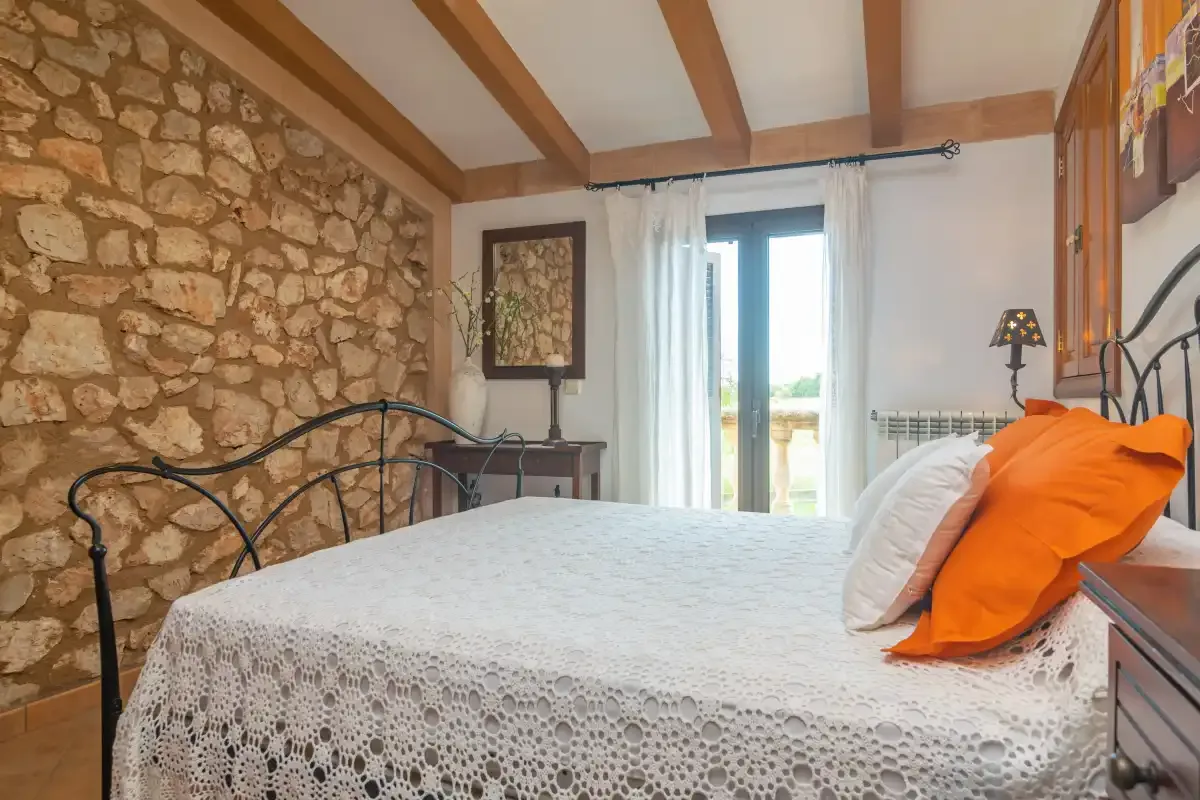 A bedroom with a bed beside a stone wall and a bright window.