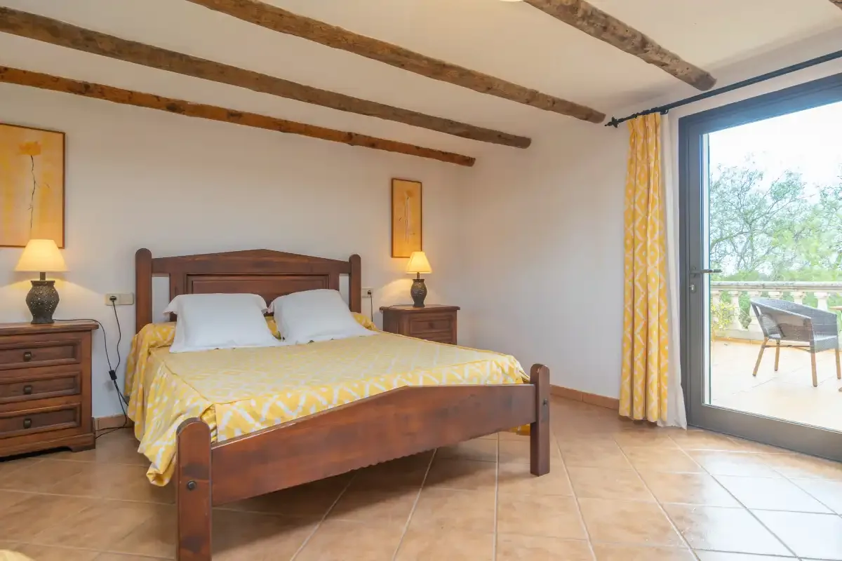 A bedroom with a wooden bed and yellow patterned bedding beside a glass door.