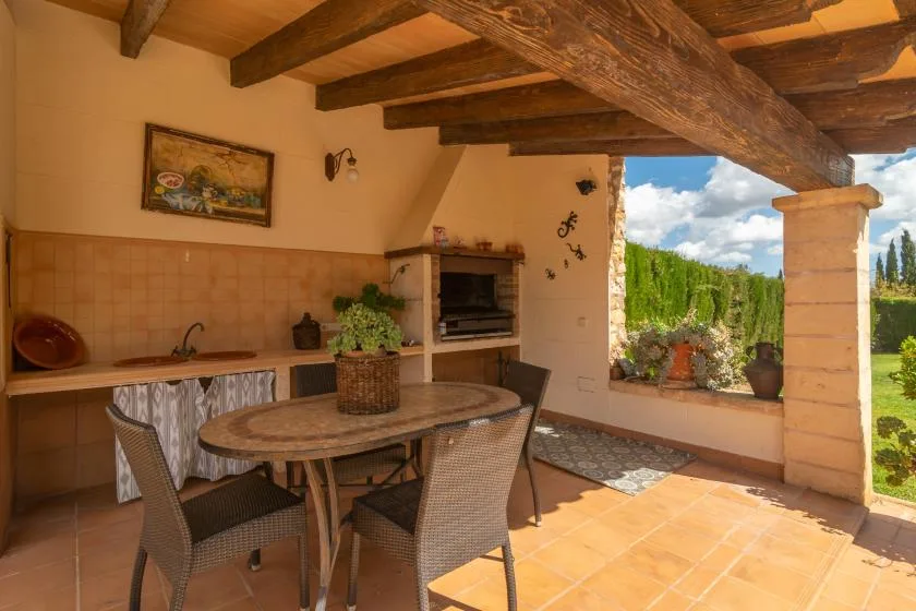 A covered outdoor dining area with a table and an open view of the garden.