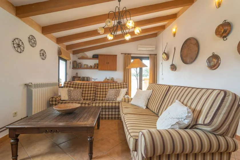 A living room with striped seating and a wooden coffee table beneath exposed ceiling beams.