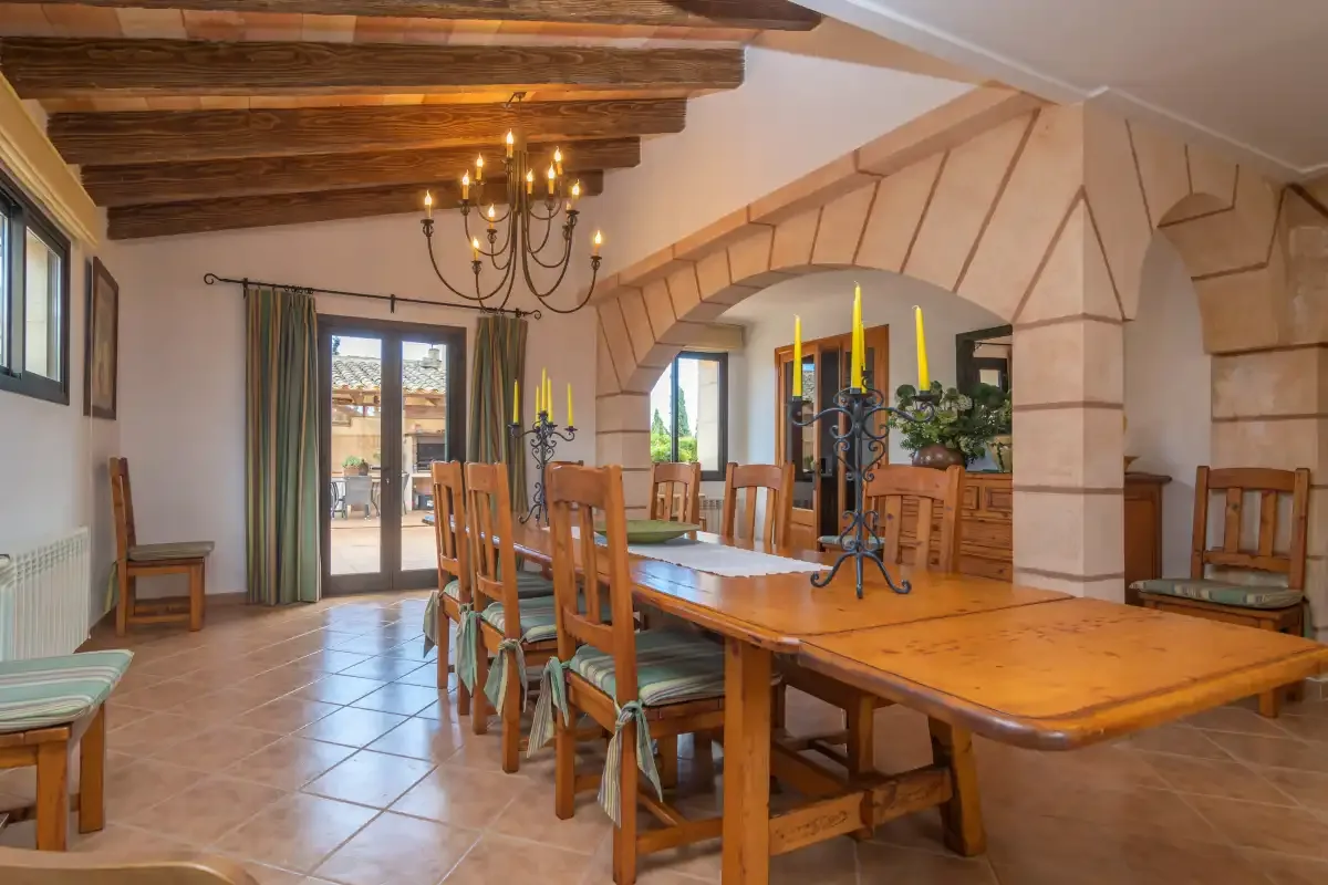 A dining room with a long wooden table beneath exposed ceiling beams.