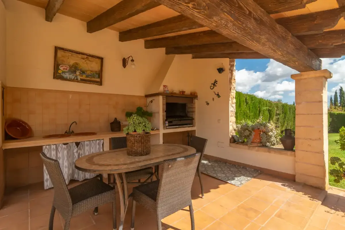 A covered outdoor dining area with a table, seating, and a built-in grill.