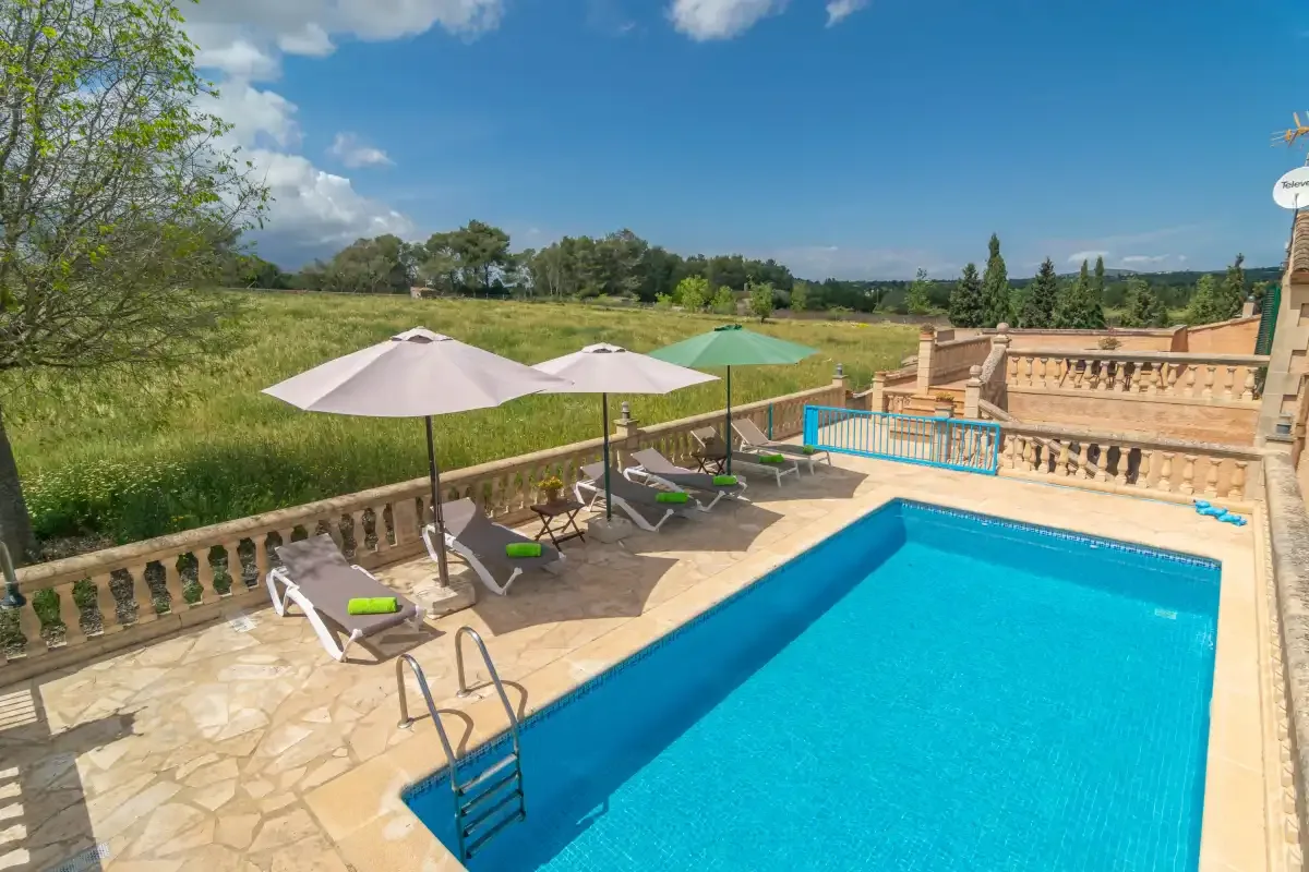 An outdoor swimming pool with lounge chairs and umbrellas beside a green landscape.