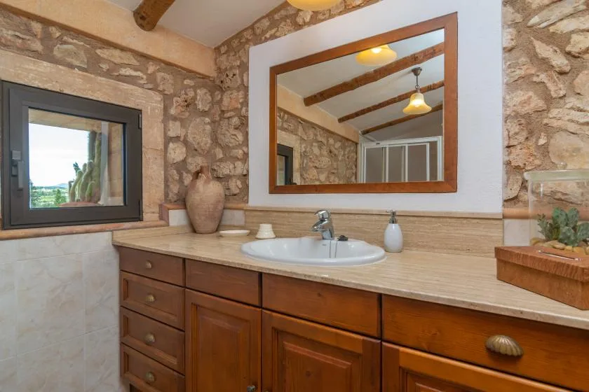 A rustic bathroom vanity with a wide mirror and stone walls.