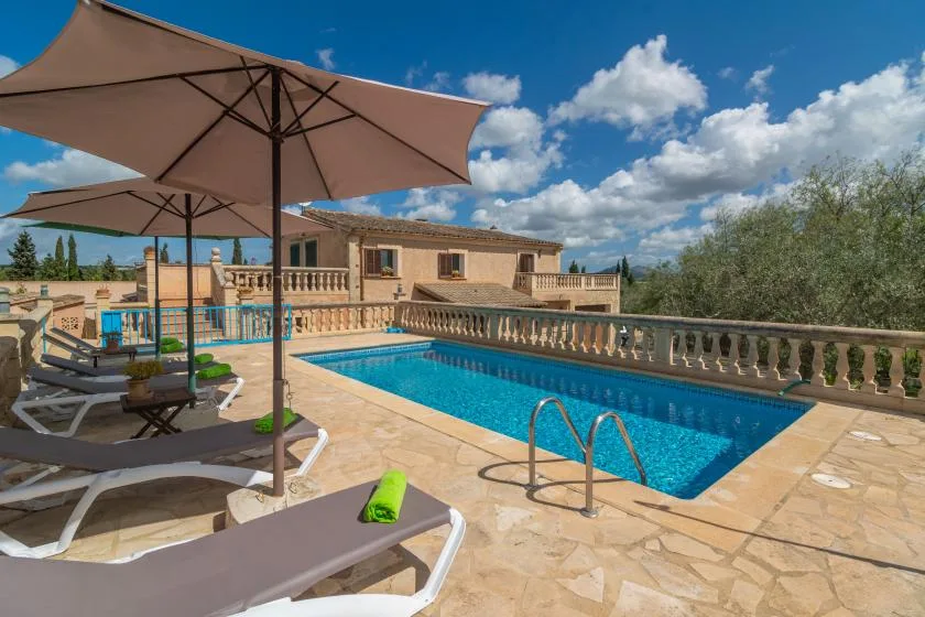 An outdoor swimming pool beside a stone terrace with shaded loungers.