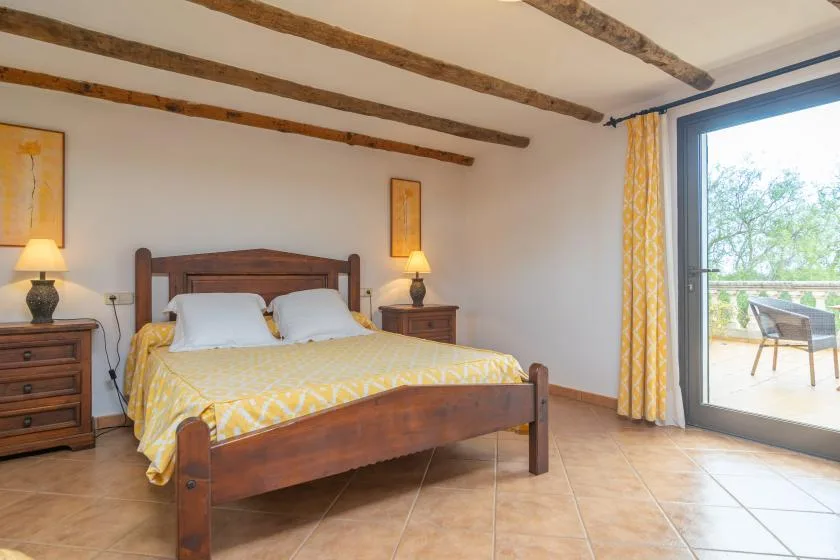 A bedroom with a wooden bed, yellow bedding, and a glass door opening onto a patio.