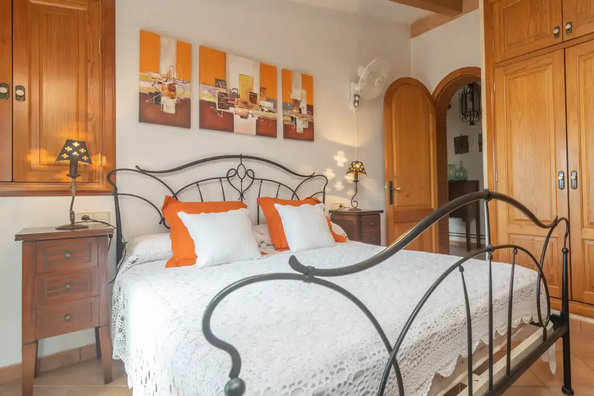 A bedroom with a bed, orange-accented pillows, and wooden cabinetry.