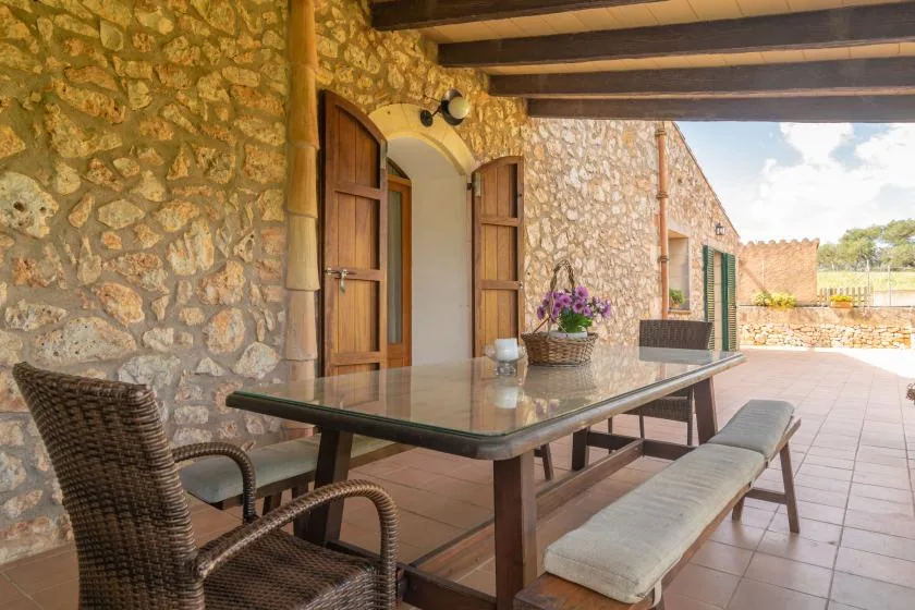 A stone patio with a dining table and seating beneath a wooden pergola.
