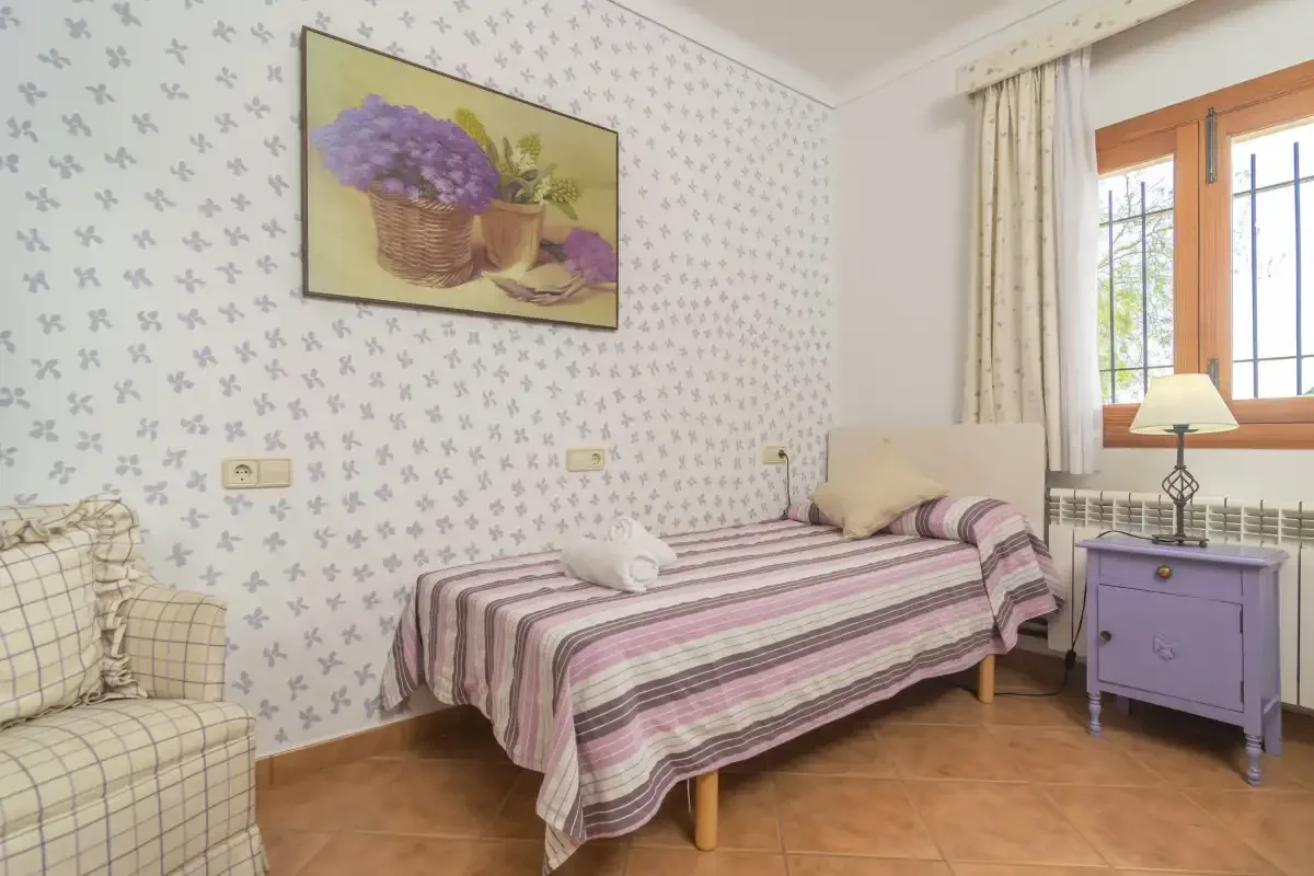 A bedroom with a striped bedspread and a window overlooking greenery.