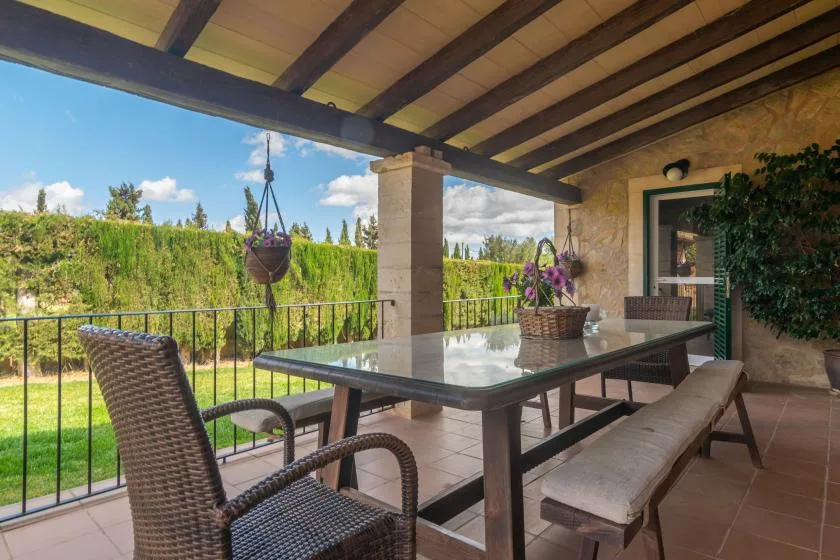 A covered patio with a table and seating overlooks a green garden.