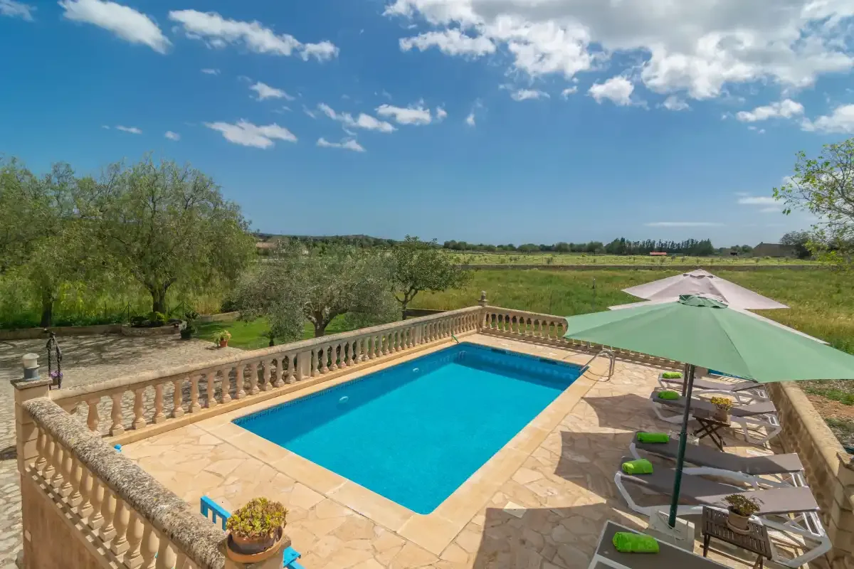 A swimming pool sits beside a paved terrace with loungers and umbrellas.