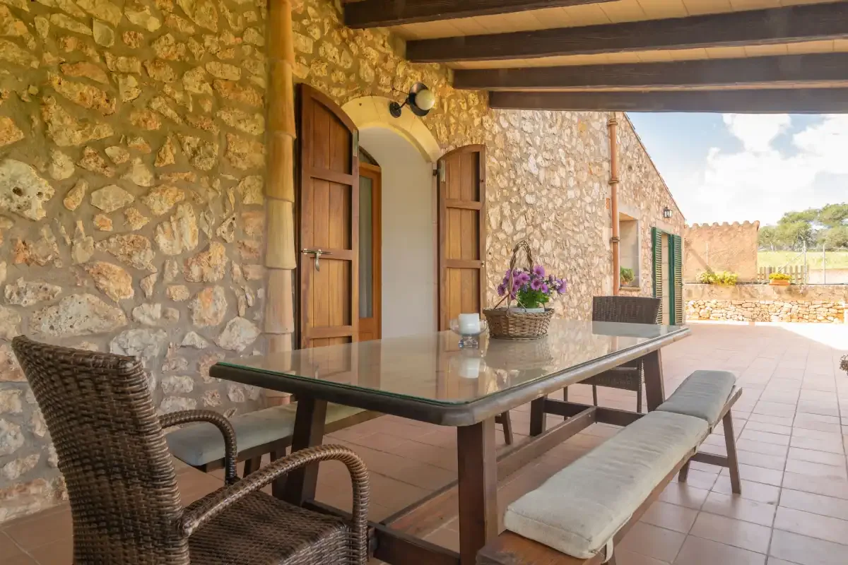 A covered stone patio with a dining table and benches.