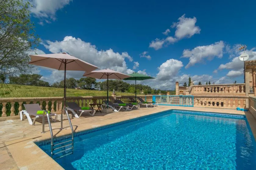 An outdoor swimming pool with umbrellas and seating along the stone terrace.