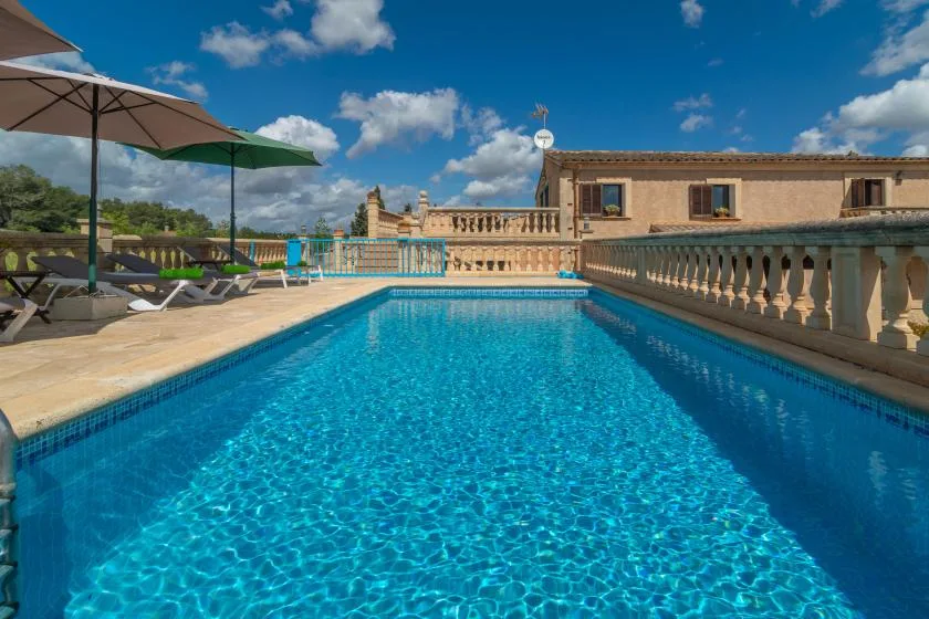 An outdoor swimming pool beside a stone terrace and shaded seating.
