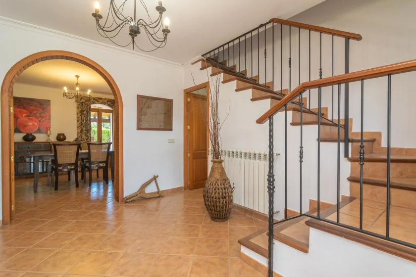 A tiled interior hallway with a staircase and an arched opening to a dining area.