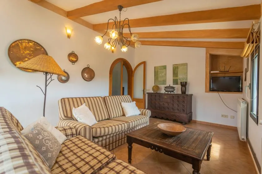 A living room with striped seating, a wooden coffee table, and exposed ceiling beams.