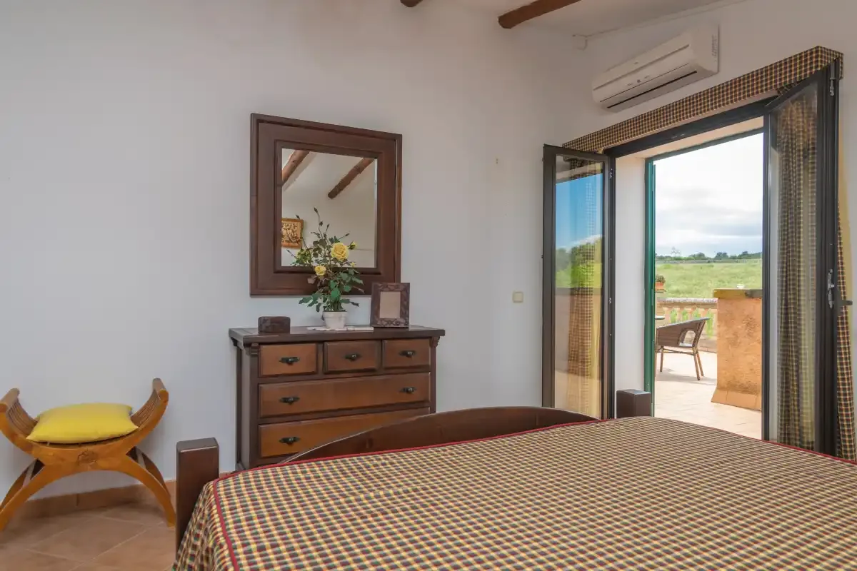 A bedroom with a bed, dresser, and open doors leading to a patio.