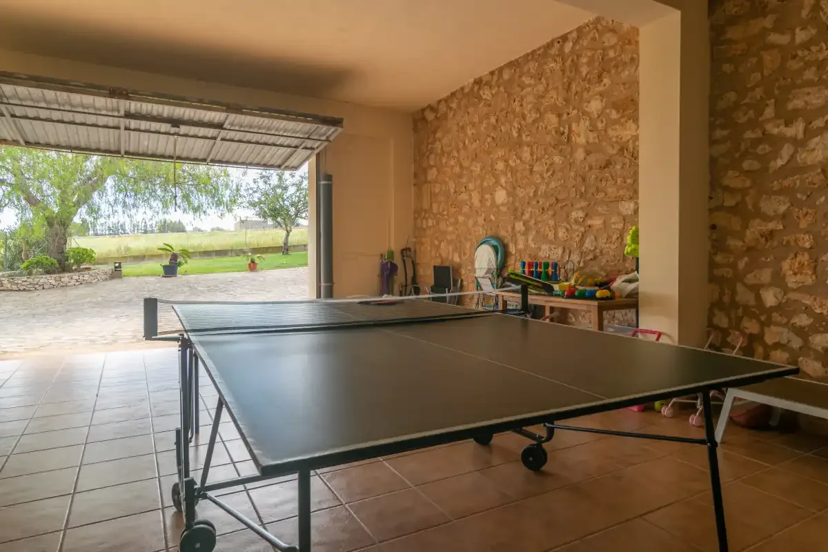 A table tennis table sits in a covered stone-walled recreation area.