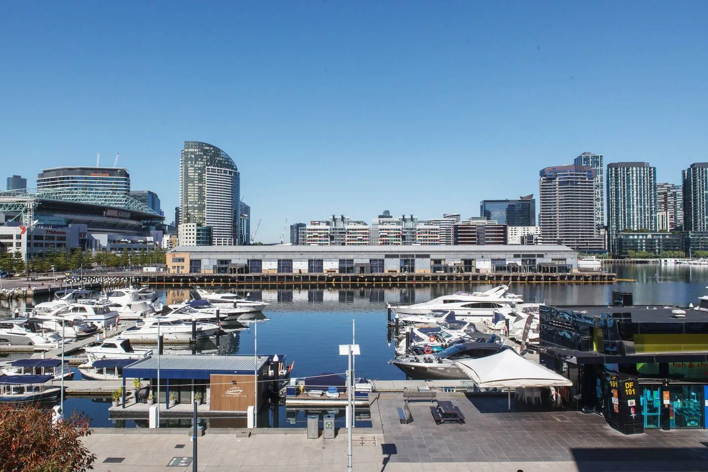 Una marina con embarcaciones amarradas se encuentra frente a un moderno horizonte urbano.