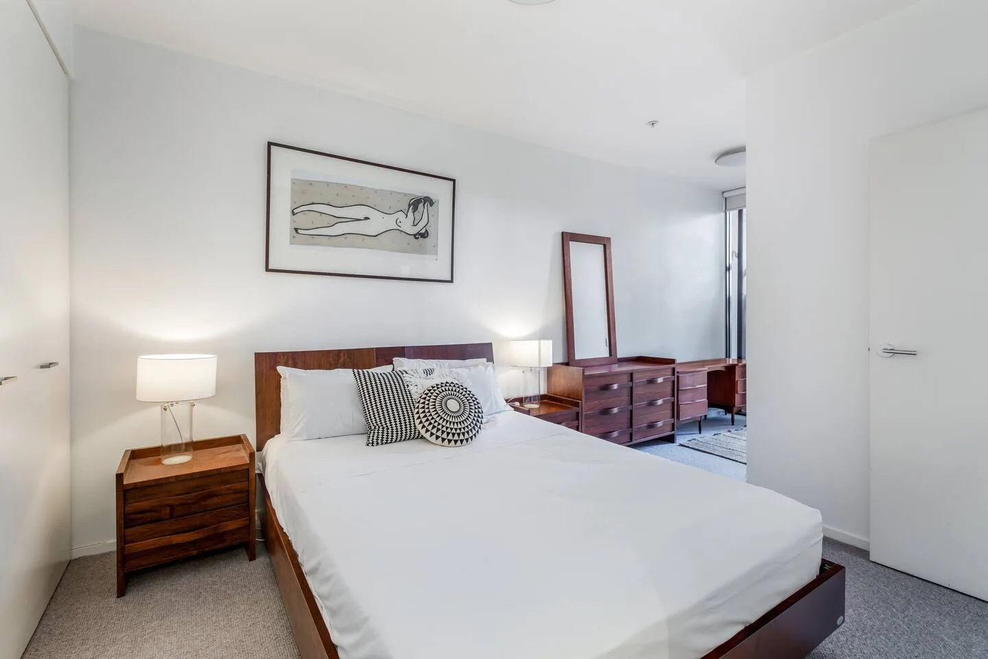 Un dormitorio luminoso con una cama bien hecha y mesitas de madera a los lados.