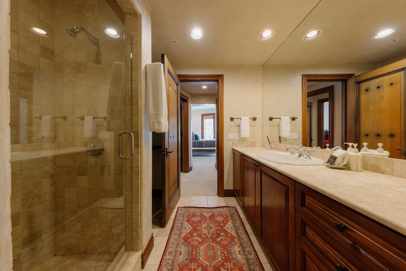 Un lavabo y una ducha de vidrio ocupan un baño con azulejos y una alfombra estampada.