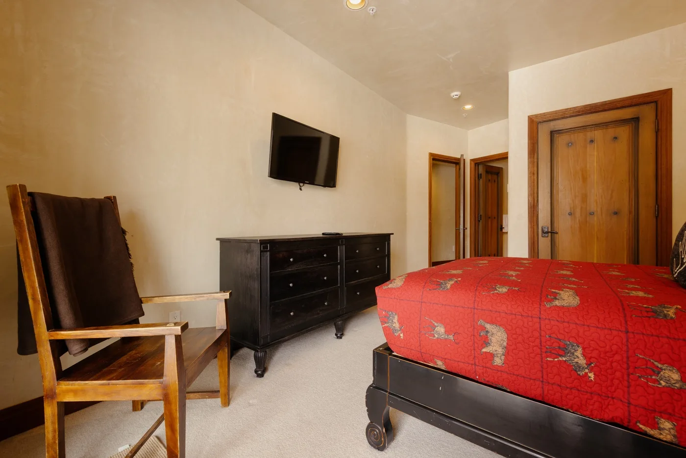 Un dormitorio con una colcha roja, una cómoda y un televisor en la pared.