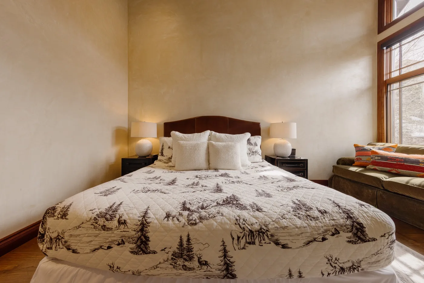 Un dormitorio con una cama grande, ropa de cama estampada y una ventana alta.