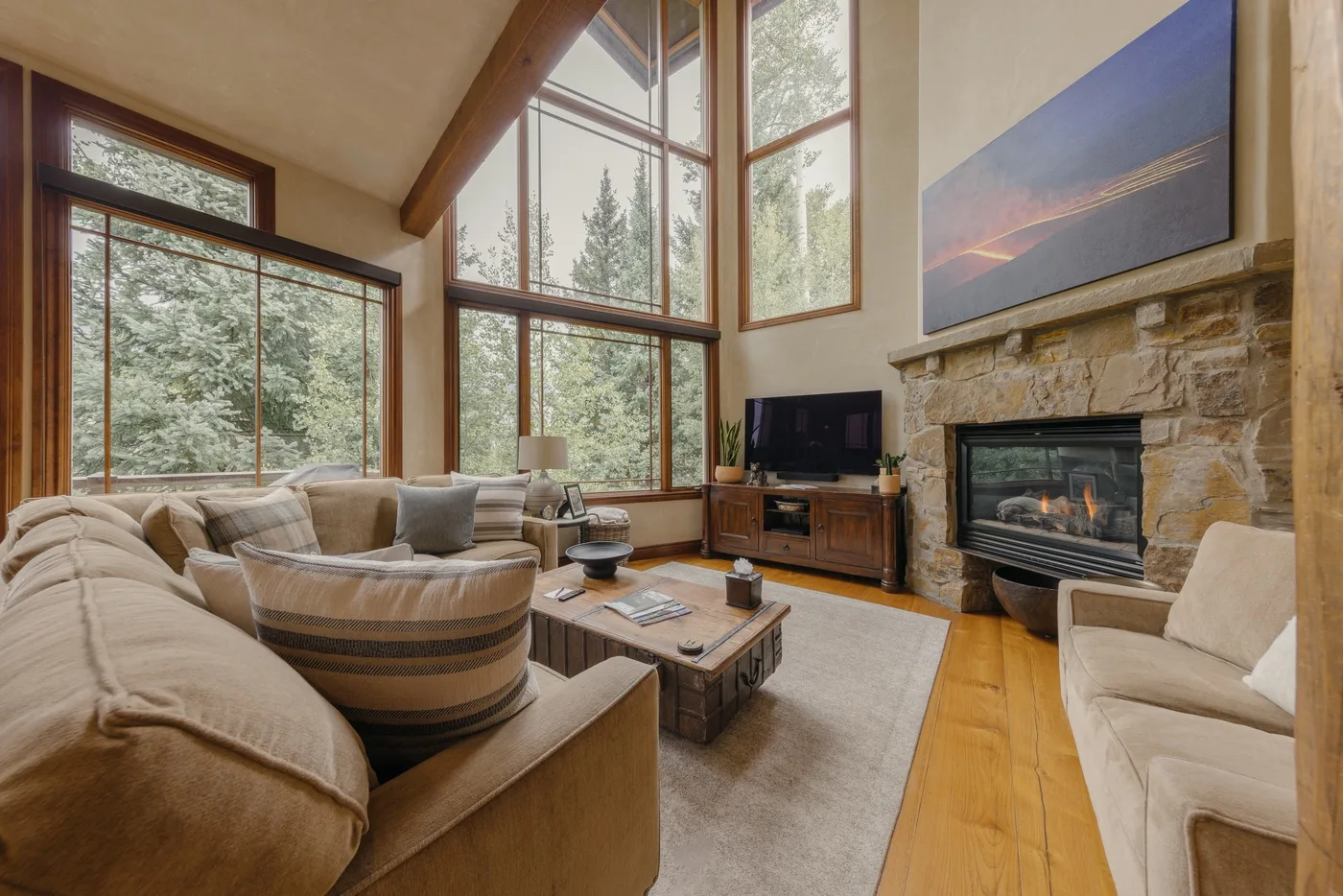 Una sala de estar con asientos, una mesa de centro y una chimenea de piedra junto a grandes ventanas.
