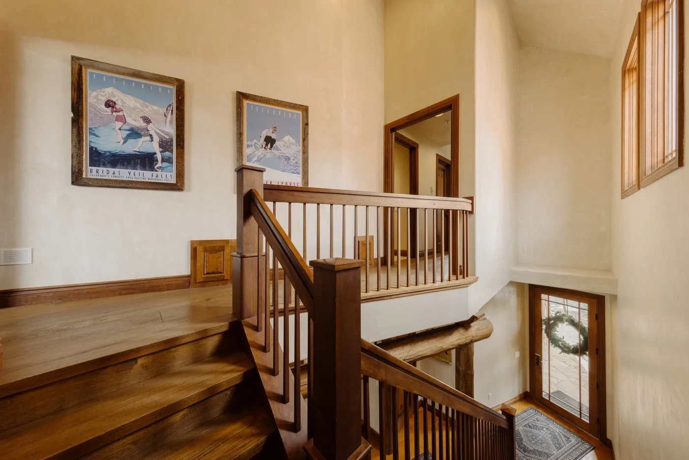 Una escalera de madera y un descansillo con cuadros en las paredes.