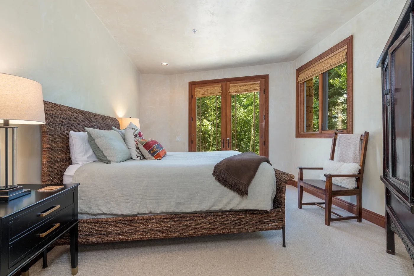 Un dormitorio con una cama de tejido, una mesa de noche y ventanas con vista a la vegetación.
