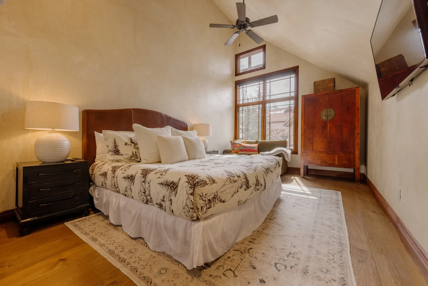 Un dormitorio con una cama grande, una mesita de noche y ventanas altas.