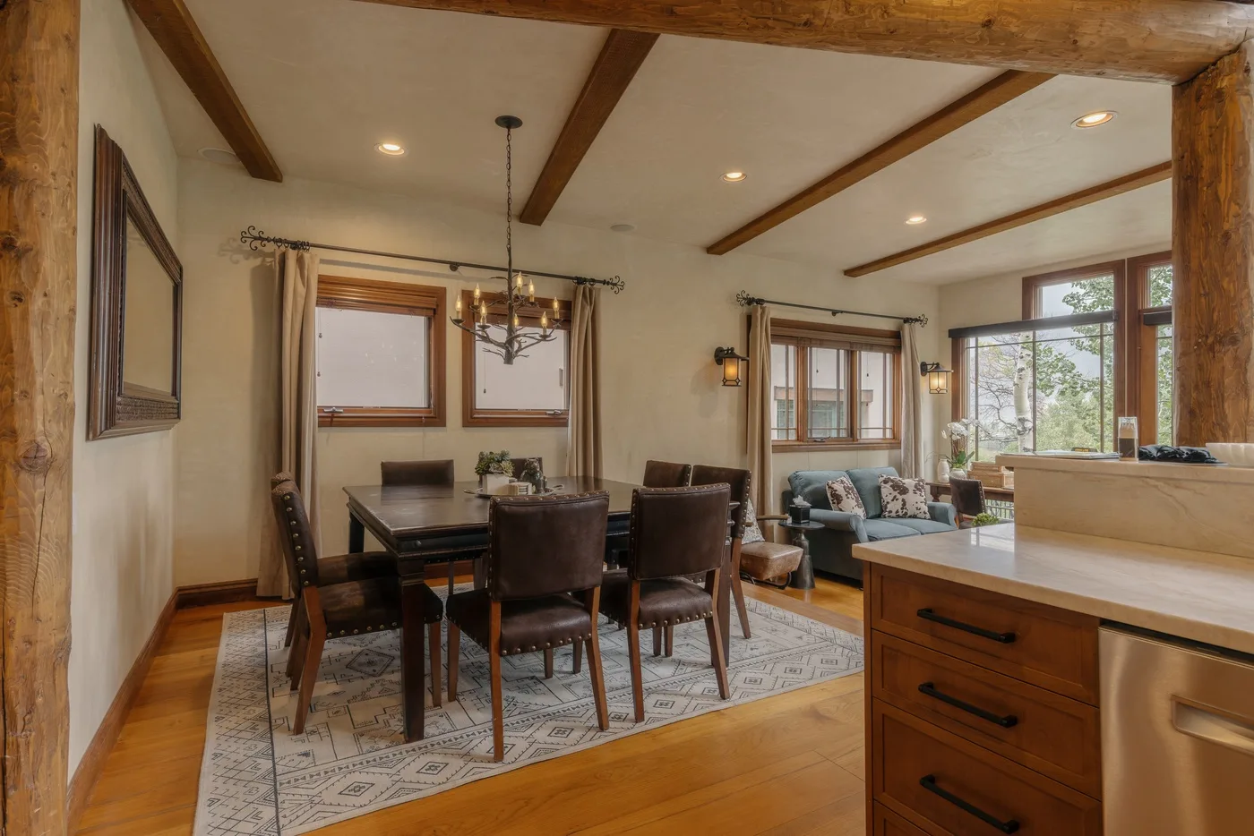 Un comedor con una mesa de madera y sillas junto a grandes ventanas.