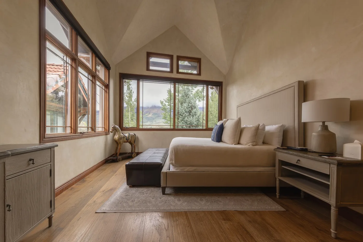 Un dormitorio con una cama grande y amplias ventanas con vistas a los árboles.