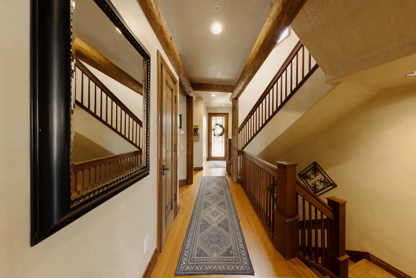 Un pasillo con suelo de madera, una alfombra estampada y una escalera a un lado.