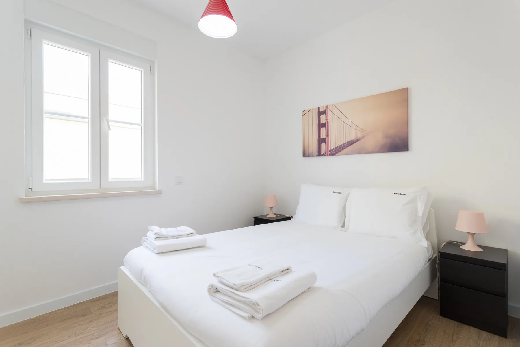 A bright bedroom with white bedding, a window, and wall art.