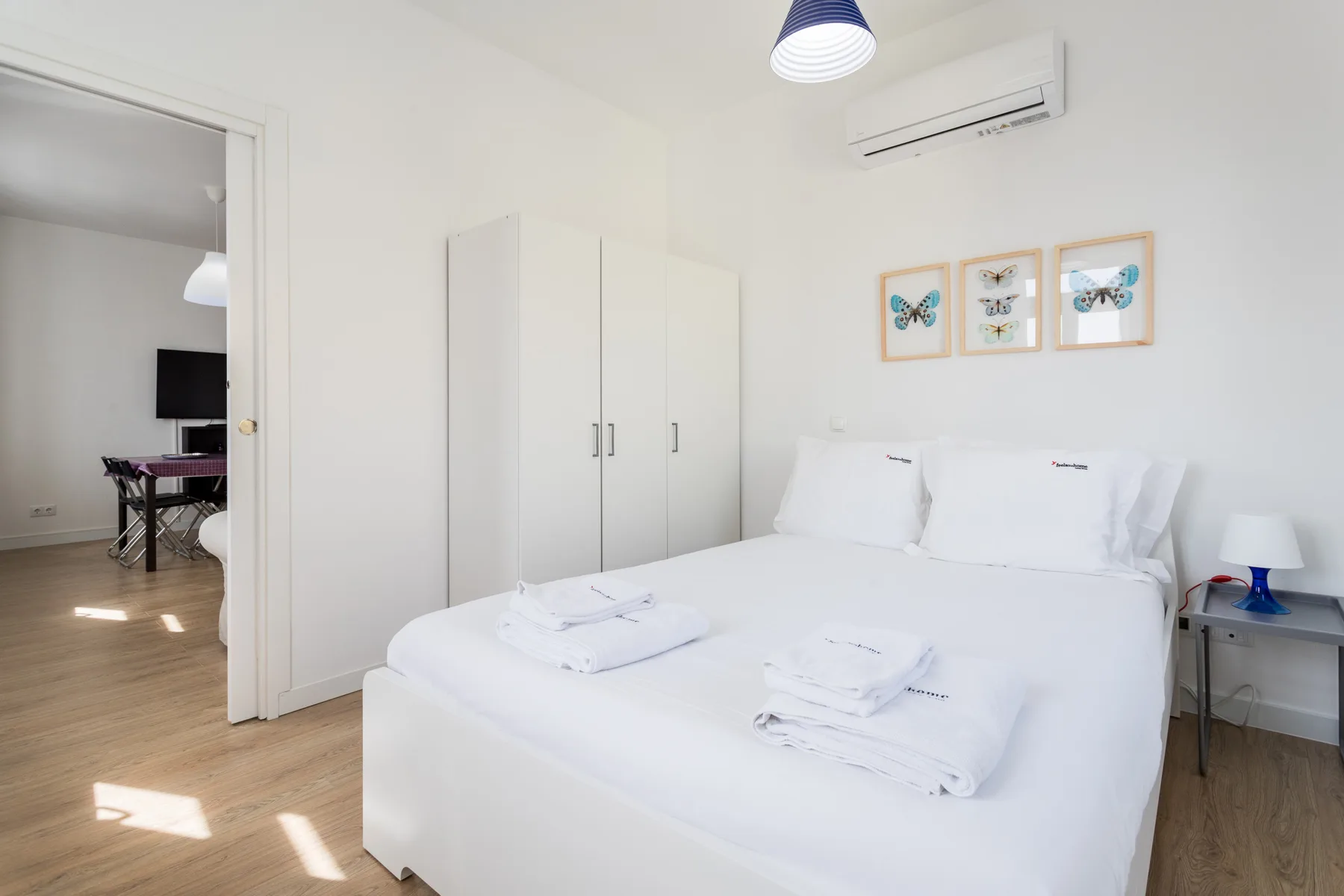 A bright bedroom with a white bed, wardrobe, and light wood flooring.
