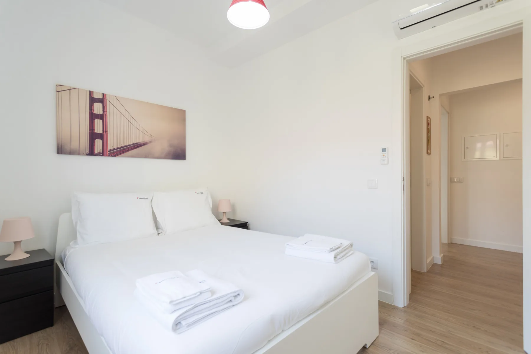 A bright bedroom with a neatly made bed and a framed bridge print.