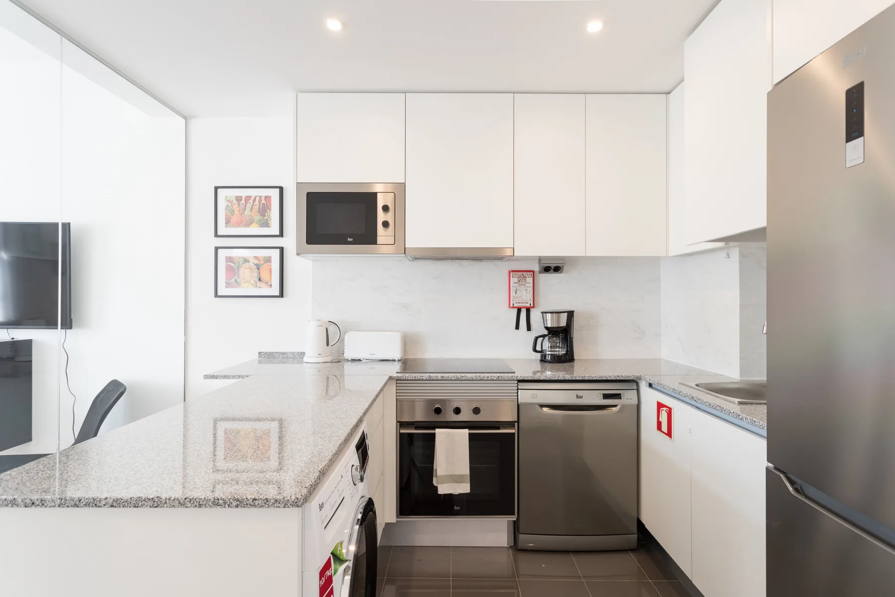 A bright modern kitchen with white cabinets, a counter, and stainless steel appliances.