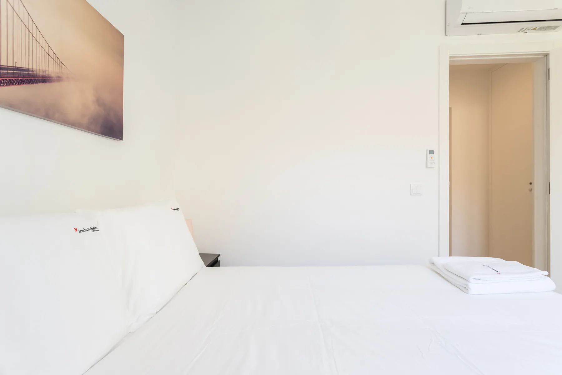 A bright bedroom with white bedding and an open doorway.