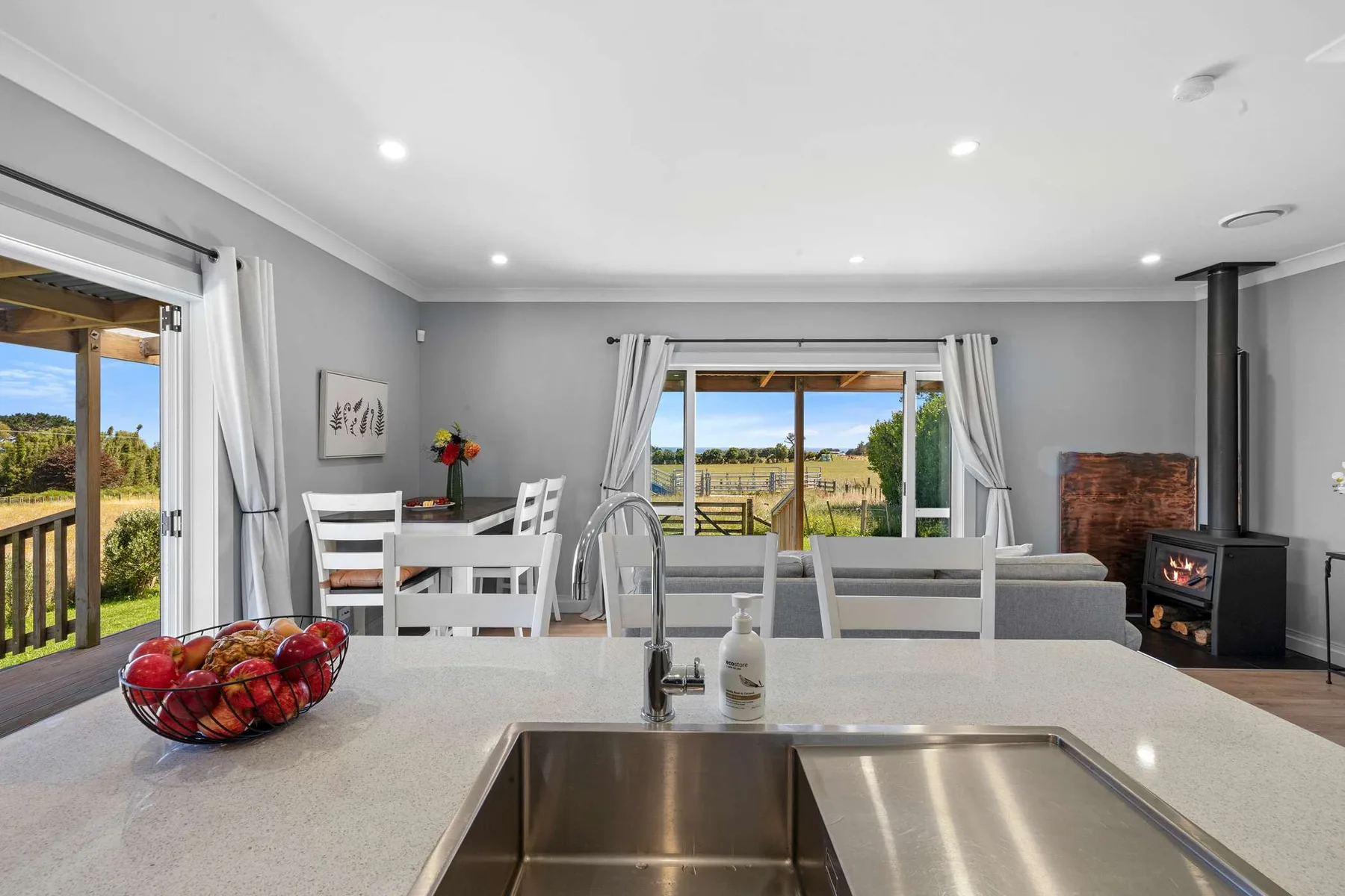 A bright open-plan kitchen and dining area overlooks a grassy landscape through large windows.